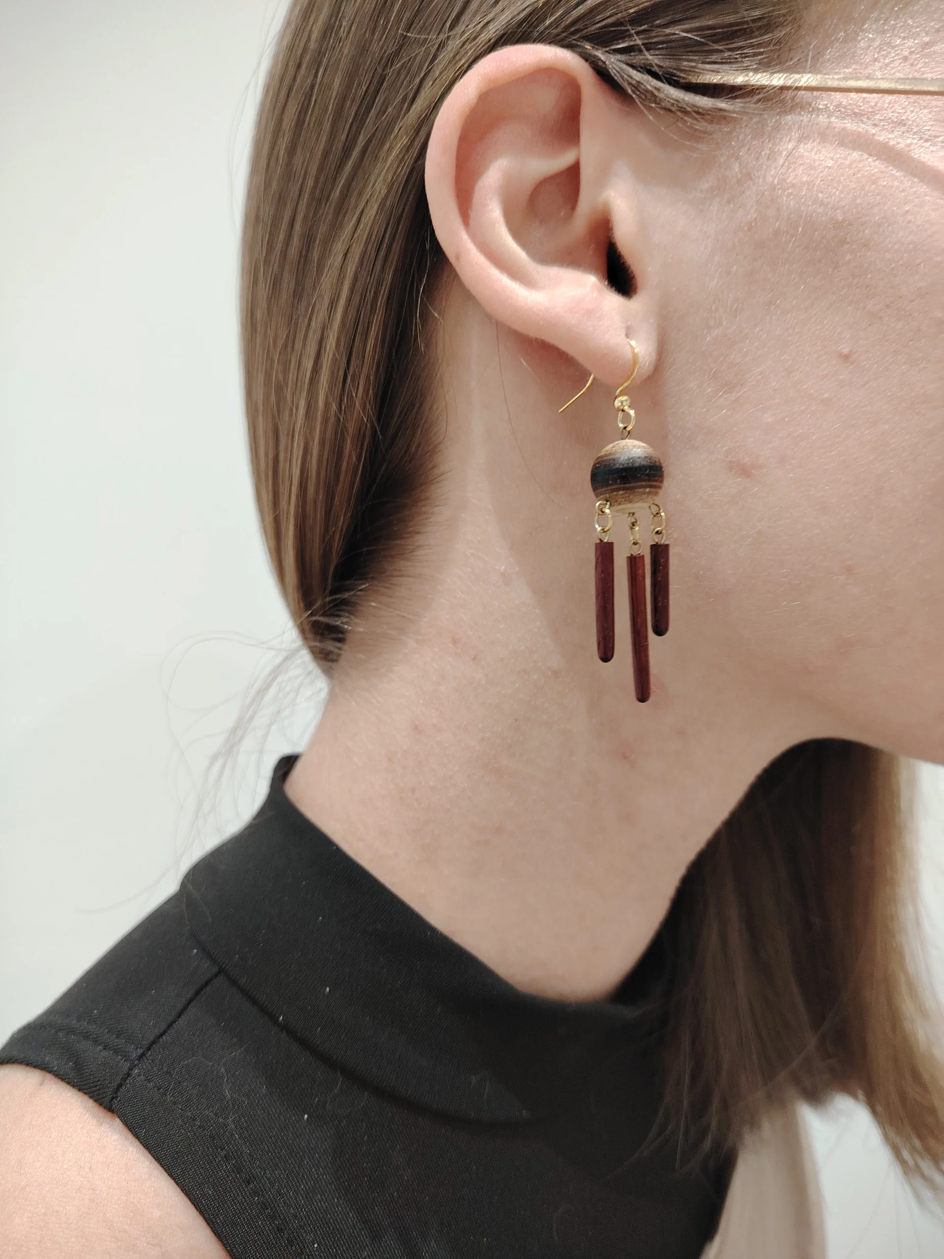 image d'une personne portant une boucle d'oreille. Celle ci est faite d'une sphère en dessous de laquelle pendent trois tige en bois rouge
